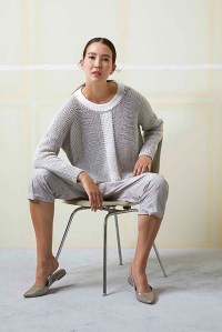 Woman wearing oversized, knitted, cotton sweater in grey with contrasting white neckline and vertical stripe down centre.