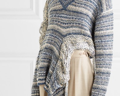 Model wears slouchy, knitted linen cotton sweater with dramatic cutouts and asymmetric hemline. Fabric is mottled blue and white stripes. From Stella McCartney Spring 2019.