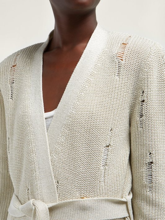 Woman wearing cream, knitted cardigan with faux rips created by lace work.
