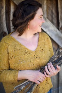 Model wearing knitted, V-neck sweater with 3/4 length sleeves, with repeats of lace triangle eyelet motif across front. Knitting pattern by Beatrice Perron Dahlen .