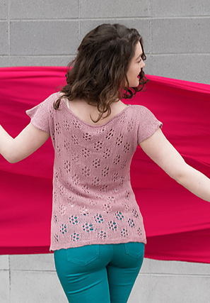 Woman wearing dusky pink, rayon/linen, knitted top with short sleeves and all over lace motif across back.