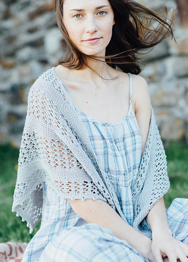 Woman wearing blue check summer dress and a hand knitted, triangular, cotton shawl with stripes of garter stitch and openwork lace.
