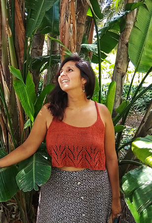 Woman standing in front of tree wearing strappy, knitted, cotton rayon tank top in warm orange colour and with chevron lace border at hem.