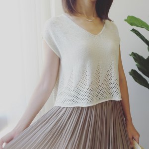 Woman wearing white, v-neck knitted cotton/rayon tee with v-neck and repeated triangle mesh lace motif around hem.