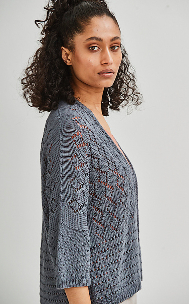 Woman wearing slate grey knitted cardigan made out of linen and with all-over lace diamond and eyelet motifs.
