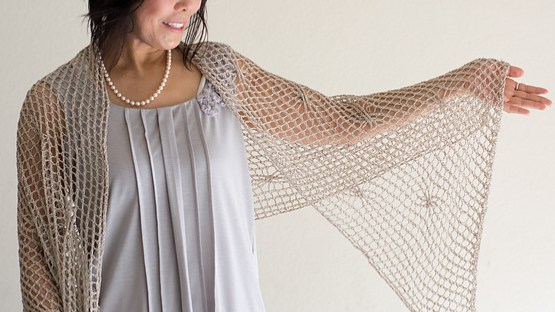 Woman wearing cream, knitted silk stole with all-over mesh texture and occasional twisted stitch that creates a small swirl in the fabric.