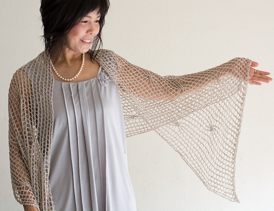 Woman wearing cream, knitted silk stole with all-over mesh texture and occasional twisted stitch that creates a small swirl in the fabric.