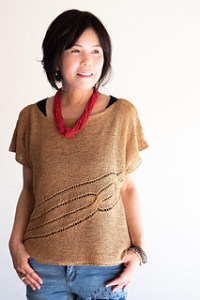 Woman wearing wide scoop neck, knitted silk/cotton top with twisted cable details across front, defined in eyelet stitches.