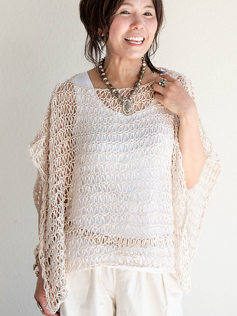 Woman wearing knitted, white poncho made in all-over, dropped stitch, open lace design.
