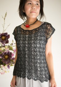Woman wearing scoop neck, short sleeved top knitted in cotton and with delicate, all-over lace design.