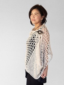 Woman wearing knitted, cotton wrap with panels of large lace eyelets, wrapped and secured at front using shawl pin.